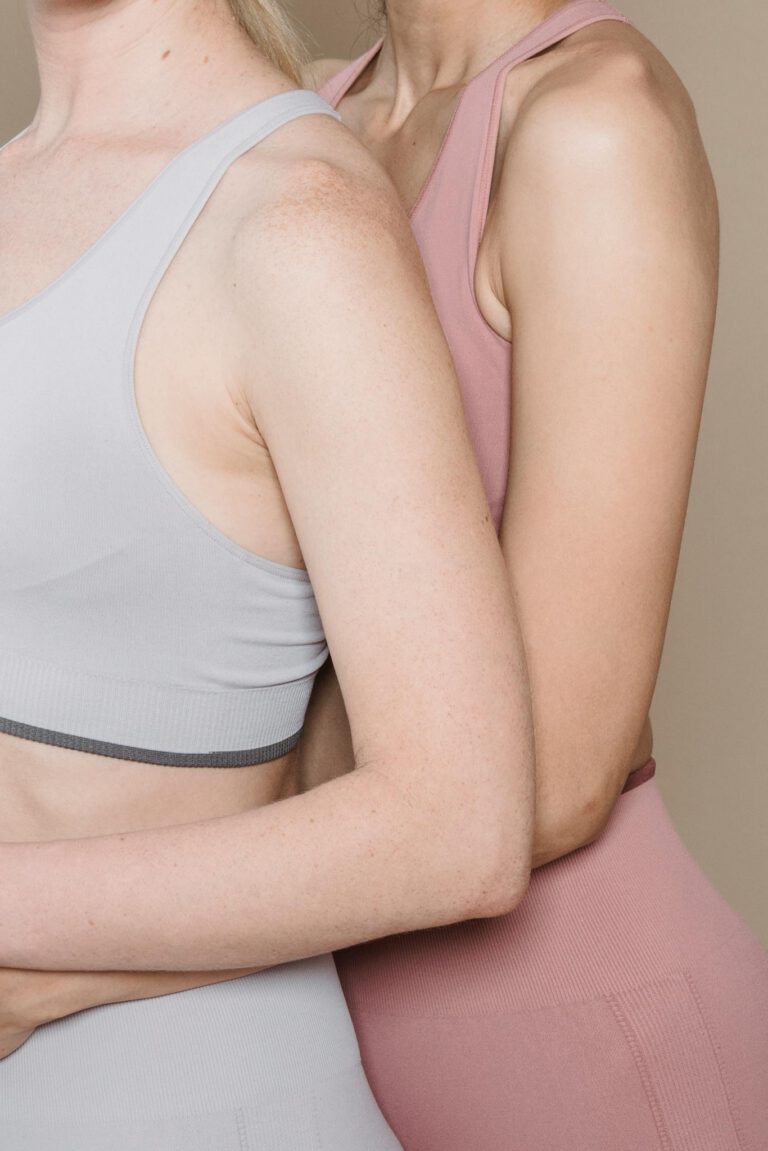 Studio shot of two women modeling modern activewear against a beige backdrop.